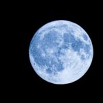 A detailed photo of a full moon with a vivid blue hue set against a black night sky.