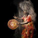 African dancer in colorful attire performing traditional tribal dance with flour explosion effect.