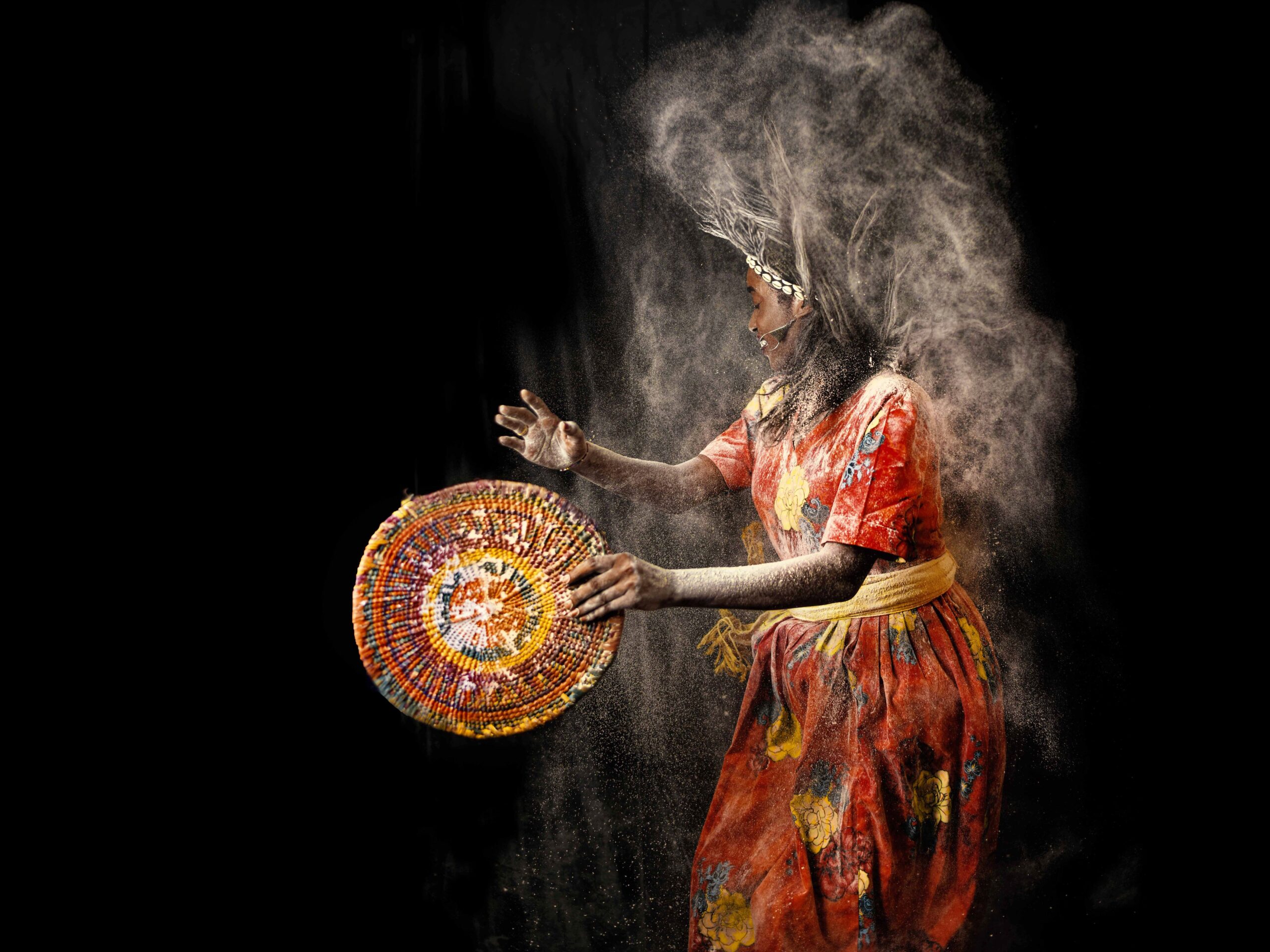African dancer in colorful attire performing traditional tribal dance with flour explosion effect.